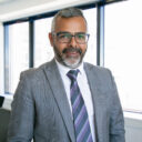 Content Indian CEO standing and smiling for portrait. Successful pensive bearded businessman in glasses posing in office room and looking at camera. Business, expression and management concept