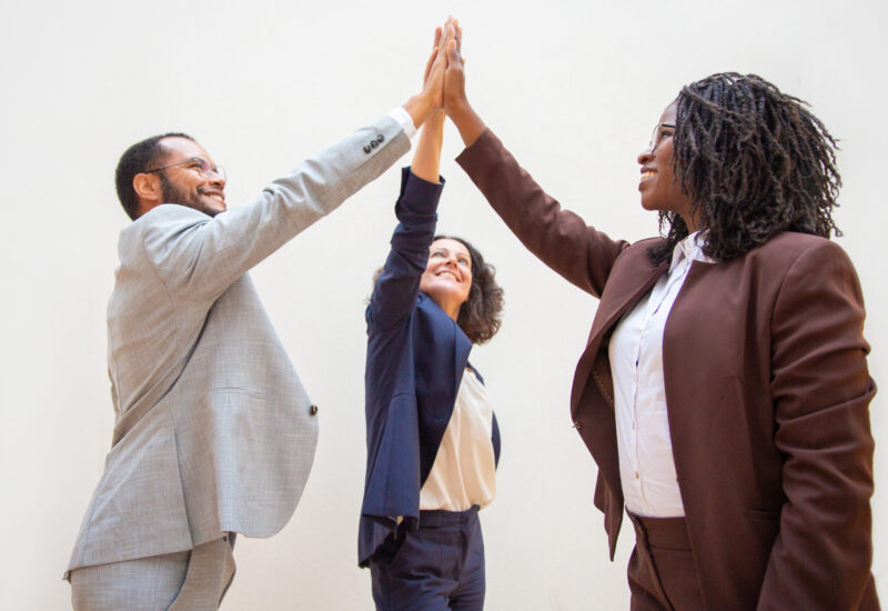 Happy business colleagues enjoying team success. Diverse group of man and women standing over white background and giving high five to each other. Achievement concept